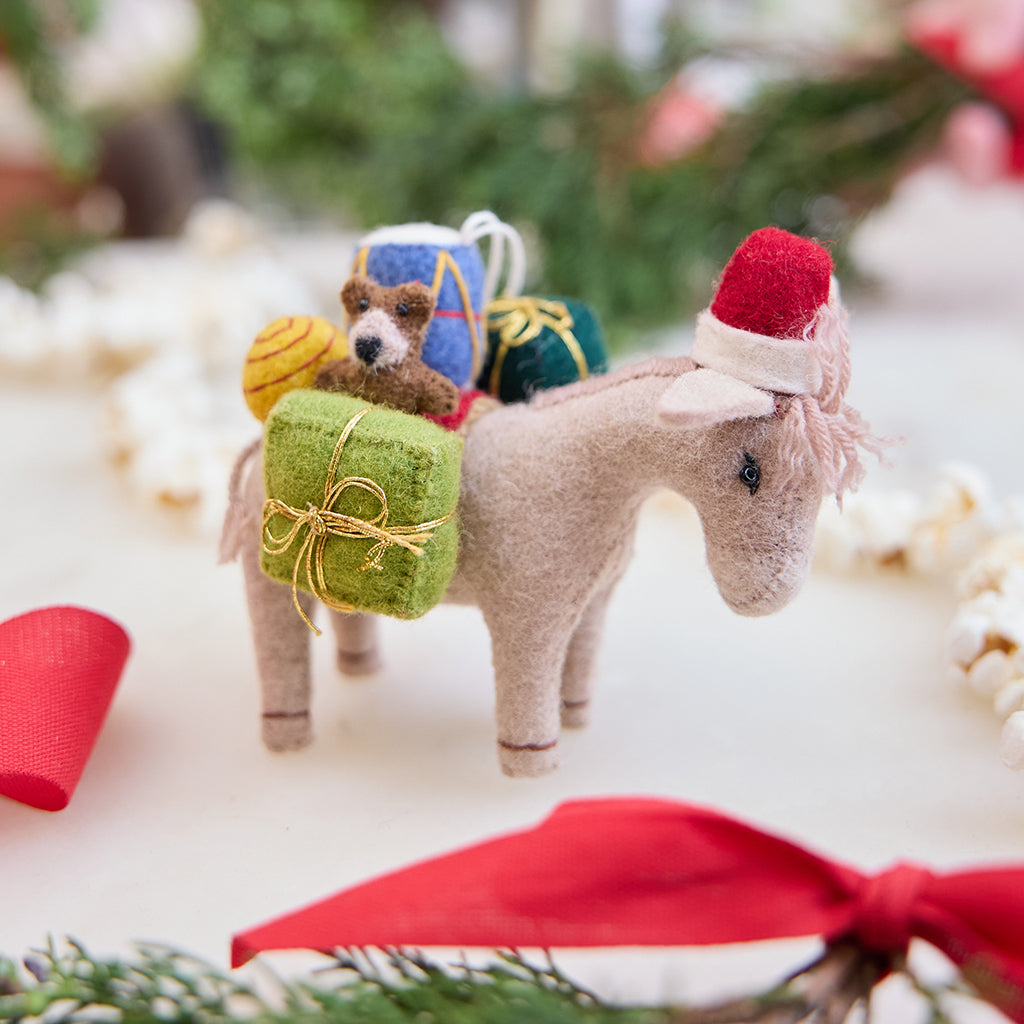 Handmade felt Donkey with Gifts ornament from Craftspring, wearing a Santa hat and carrying toys—displayed among evergreens and a popcorn garland, perfect for Christmas gifting and festive decor, ethically crafted by artisans using sustainable wool.