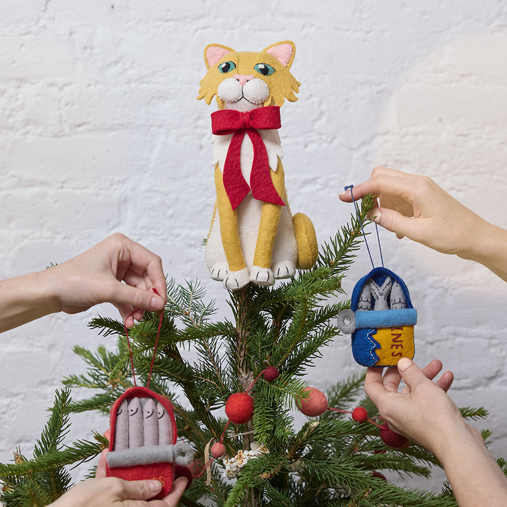 Handmade felt Orange Cat Tree Topper from Craftspring, wearing a festive red bow—perched atop a Christmas tree decorated with playful sardine ornaments, adding whimsical holiday charm and purr-fect gifting joy, ethically crafted by artisans using sustainable wool.