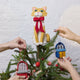 Handmade felt Orange Cat Tree Topper from Craftspring, wearing a festive red bow—perched atop a Christmas tree decorated with playful sardine ornaments, adding whimsical holiday charm and purr-fect gifting joy, ethically crafted by artisans using sustainable wool.