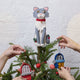 Handmade felt Gray Cat Tree Topper from Craftspring, featuring holly accents and a red collar with a bell—displayed on a Christmas tree decorated with sardine ornaments, perfect for cat lovers and playful holiday decorating, ethically crafted by artisans using sustainable wool.