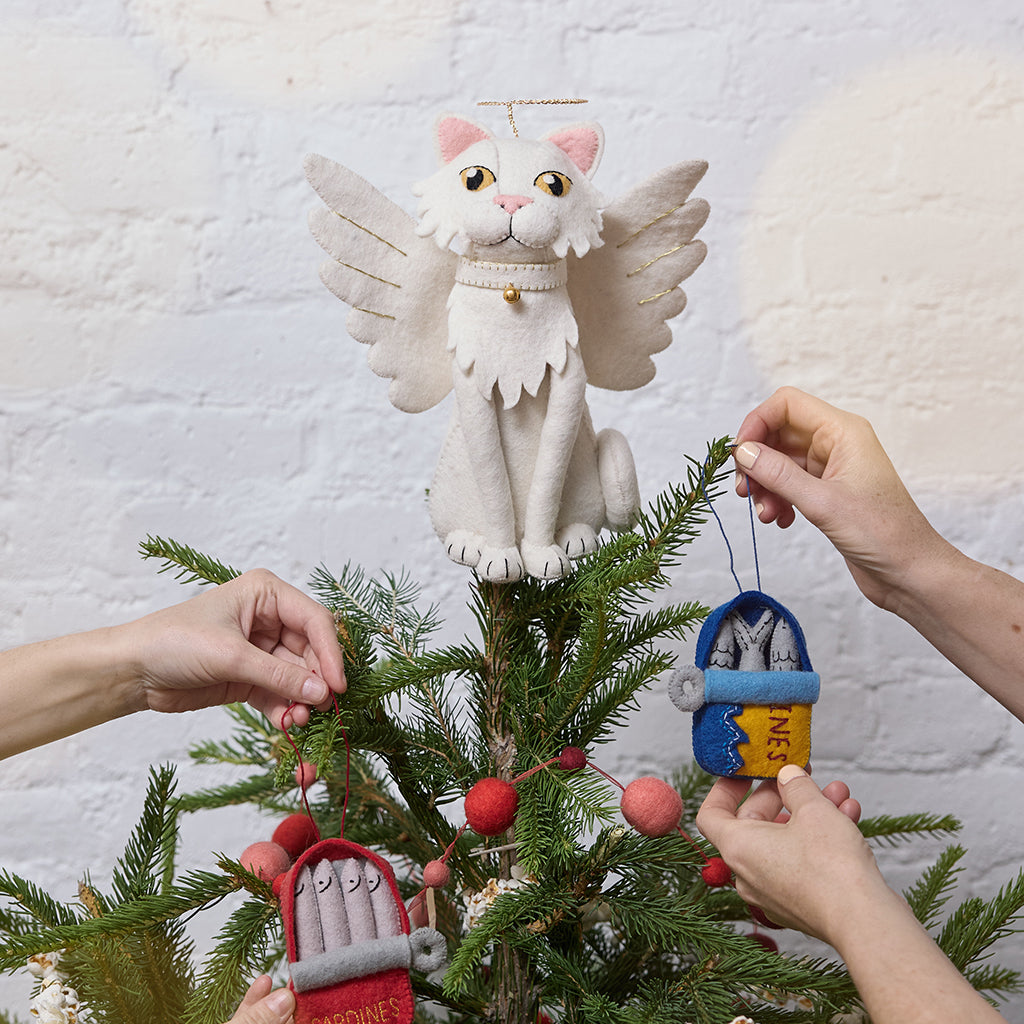 Handmade felt Angel Cat Tree Topper from Craftspring, featuring white angel wings, a halo, a white collar with a bell, and gold embroidered details—displayed on a Christmas tree decorated with playful sardine ornaments, perfect for whimsical holiday charm and thoughtful gifting, ethically crafted by artisans using sustainable wool.