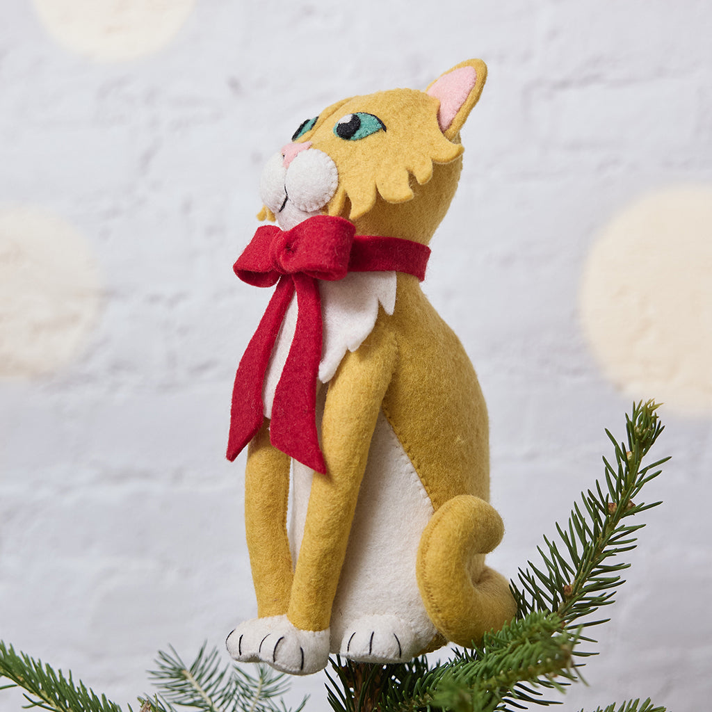 Handmade felt Orange Cat Tree Topper from Craftspring, wearing a festive red bow—shown from the side perched atop a Christmas tree, bringing playful holiday cheer and purr-fect gifting joy, ethically crafted by artisans using sustainable wool.
