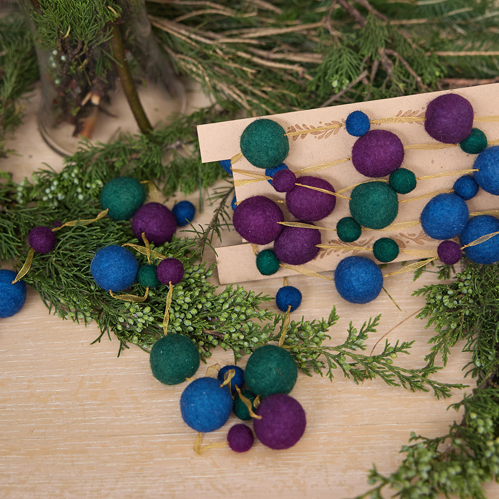 Handmade felt Jewel Tone Ball Garland from Craftspring, featuring deep jewel-tone felt balls strung on a gold ribbon—displayed among evergreen branches, perfect for adding rich, festive color and heirloom-quality holiday charm, ethically crafted by artisans using sustainable wool.