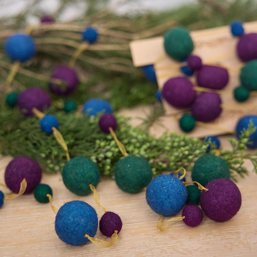 Handmade felt Jewel Tone Ball Garland from Craftspring, featuring deep jewel-tone felt balls strung on a gold ribbon—displayed among evergreen branches, perfect for adding rich, festive color and heirloom-quality holiday charm, ethically crafted by artisans using sustainable wool.