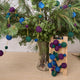 Handmade felt Jewel Tone Ball Garland from Craftspring, featuring deep jewel-tone felt balls strung on a gold ribbon—displayed among evergreen branches, perfect for adding rich, festive color and heirloom-quality holiday charm, ethically crafted by artisans using sustainable wool.