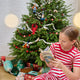 Craftspring’s Maine-themed ornaments, including shells, a lobster, lobsterman, fisherman, lighthouse, seagull, and hermit crab, displayed on a Christmas tree with presents below — a girl in Christmas pajamas reading nearby, creating a cozy holiday scene with gifting warmth, ethically crafted by artisans.