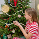 Craftspring’s Maine-themed ornaments, including Lobster, Lobsterman, Fisherman, Oyster, Moon Snail Shell, Scallop Shell, and Hermit Crab, displayed on a Christmas tree with presents below — a girl in Christmas pajamas admiring the Hermit Crab ornament, creating a cozy and festive holiday scene with gifting warmth, ethically crafted by artisans.