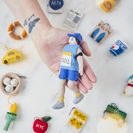 Craftspring’s handmade felt Marathon Runner ornament — featuring a runner with a race bib numbered 001 and an armband, held in hand above the NYC Mini Ornaments Set of 24 for a festive holiday scene, perfect for Christmas decorating or gifting, ethically crafted by artisans using sustainable wool.