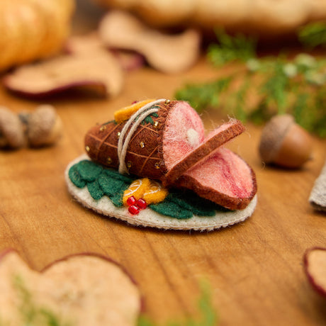 Craftspring’s handmade felt Spiral Ham Platter ornament — a festive ham with intricate beaded and embroidered details, displayed on a harvest table with dried apple slices and pumpkins for a warm holiday scene, perfect for Thanksgiving decorating or gifting, ethically crafted by artisans using sustainable wool.