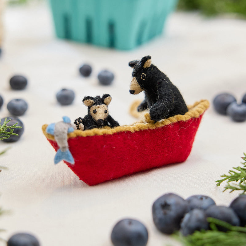 Craftspring’s handmade felt Bears in a Canoe ornament — a mama bear paddling a canoe with a cub climbing over the side, displayed with evergreens and blueberries for a whimsical holiday scene, perfect for Christmas decorating or gifting, ethically crafted by artisans using sustainable wool.