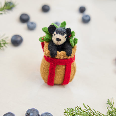 Craftspring’s handmade felt Adirondack Basket with Black Bear Cub ornament — a cozy brown basket with a playful black bear cub peeking out, displayed with evergreens and blueberries for a rustic holiday touch, perfect for Christmas decorating or gifting, ethically crafted by artisans using sustainable wool.