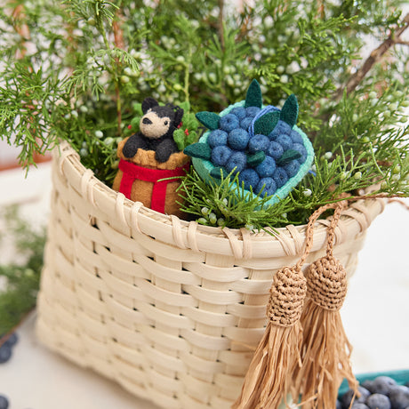 Craftspring’s handmade felt Adirondack Basket with Black Bear Cub and Blueberry Pint ornaments — a black bear cub in a cozy basket and a pint of blueberries, displayed in a handwoven basket with juniper for a festive holiday scene, perfect for Christmas decorating or gifting, ethically crafted by artisans using sustainable wool.