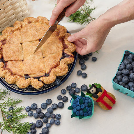 Craftspring’s handmade felt Adirondack Basket with Black Bear Cub and Blueberry Pint ornaments — a playful black bear cub peeking from a cozy brown basket and a pint of plump blueberries, displayed with a blueberry pie for a warm, festive holiday scene, perfect for Christmas decorating or gifting, ethically crafted by artisans using sustainable wool