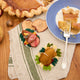Craftspring’s handmade felt Spiral Ham Platter and Turkey Dinner ornaments — a festive ham with intricate beaded and embroidered details and a roasted turkey with autumn sides, displayed on a harvest table with pumpkin pie for a cozy holiday scene, perfect for Thanksgiving decorating or gifting, ethically crafted by artisans using sustainable wool.