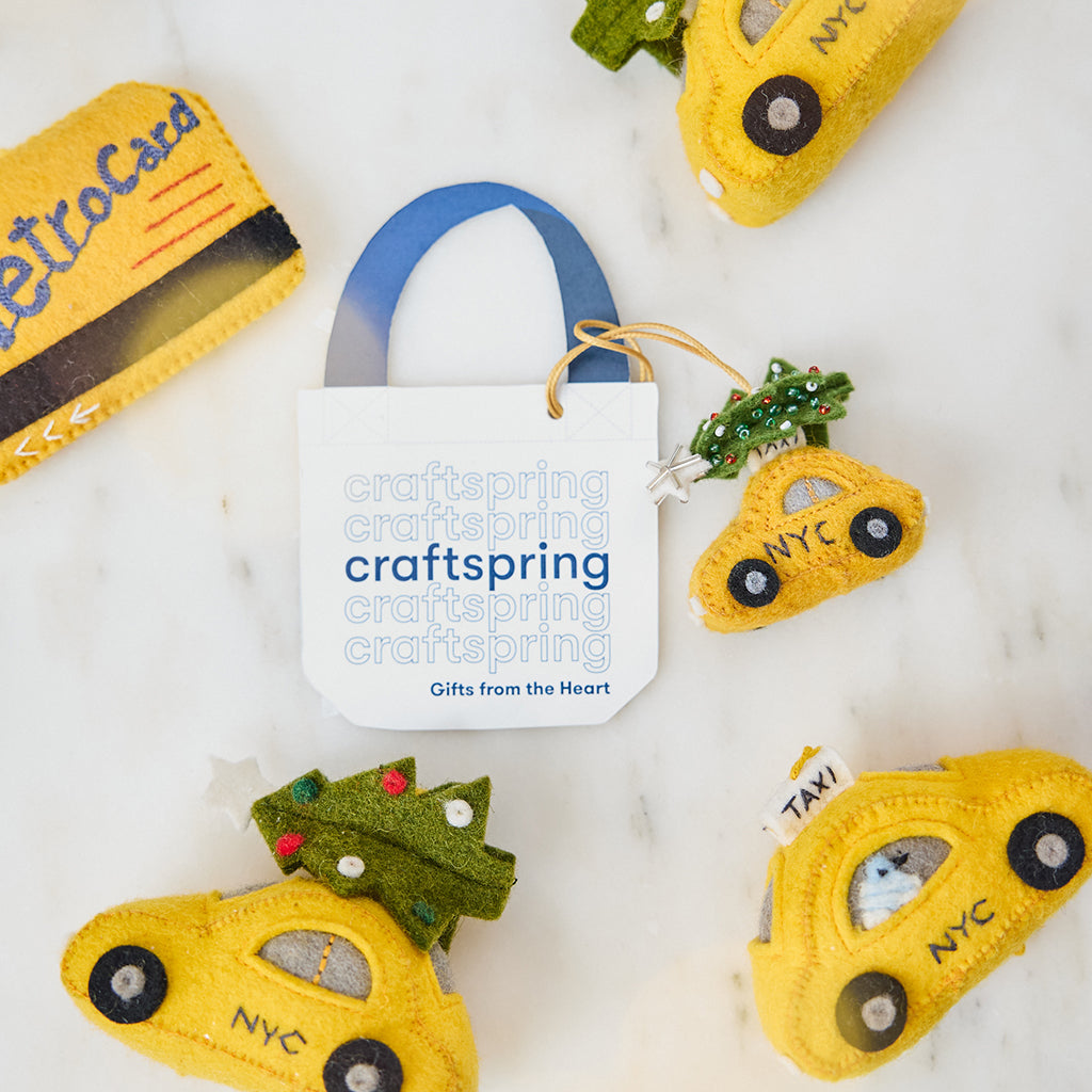 Craftspring’s Holiday Taxi Bag Charm — handmade felt taxi with a beaded Christmas tree — styled among Craftspring’s NYC-themed ornaments including the Holiday Taxi and Metro Card, capturing whimsical holiday spirit, heirloom-quality charm, and gifting joy, ethically crafted by women artisans in Kyrgyzstan using locally sourced wool.