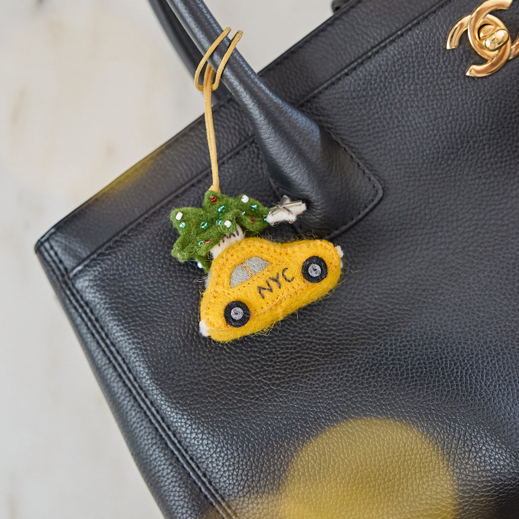 Craftspring’s Holiday Taxi Bag Charm — handmade felt taxi with a beaded Christmas tree — displayed on a black Chanel bag, adding playful holiday charm and heirloom-quality cheer, ethically crafted by women artisans in Kyrgyzstan using locally sourced wool.