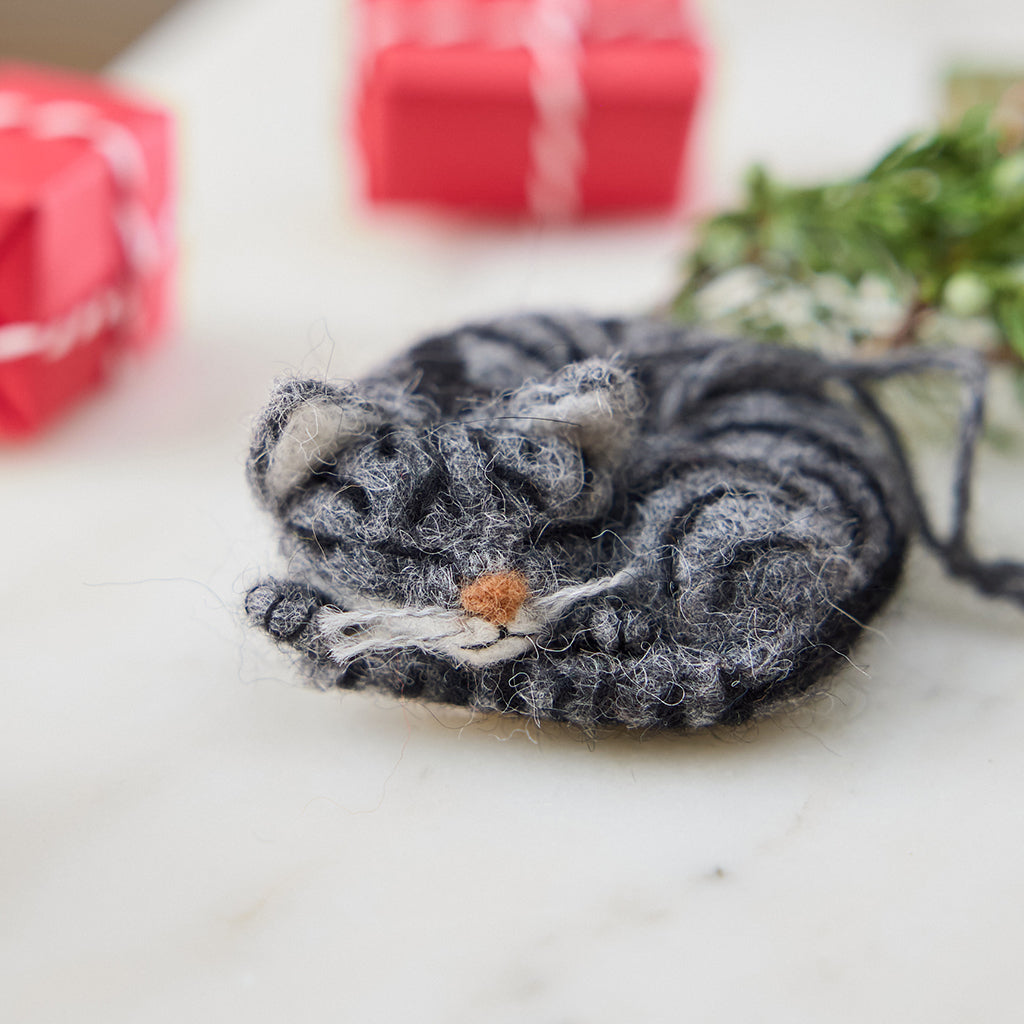 Craftspring’s needle-felted Sleepy Gray Cat Ornament displayed with evergreens and mini presents — with whiskers and a cute face, creating a cozy and festive holiday scene, perfect for gifting, ethically crafted by artisans using sustainable wool.