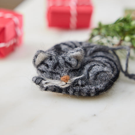 Craftspring’s needle-felted Sleepy Gray Cat Ornament displayed with evergreens and mini presents — with whiskers and a cute face, creating a cozy and festive holiday scene, perfect for gifting, ethically crafted by artisans using sustainable wool.