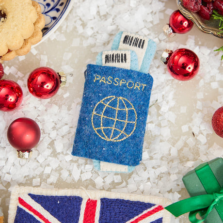 Craftspring’s handmade felt Passport ornament — featuring applique and embroidered details with two plane tickets tucked inside and passport stamps on the back, displayed with Christmas baubles and mini presents for a festive holiday scene, perfect for Christmas decorating or gifting, ethically crafted by artisans using sustainable wool.