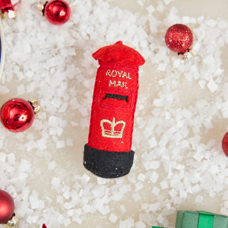 Craftspring’s handmade felt British Post Box ornament — classic red design with gold embroidered details, displayed in snow with Christmas baubles for a festive holiday scene, perfect for Christmas decorating or gifting, ethically crafted by artisans using sustainable wool.