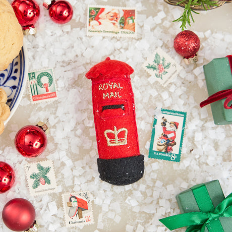 Craftspring’s handmade felt British Post Box ornament — classic red design with gold embroidered details, displayed with vintage Christmas stamps for a nostalgic holiday scene, perfect for Christmas decorating or gifting, ethically crafted by artisans using sustainable wool.