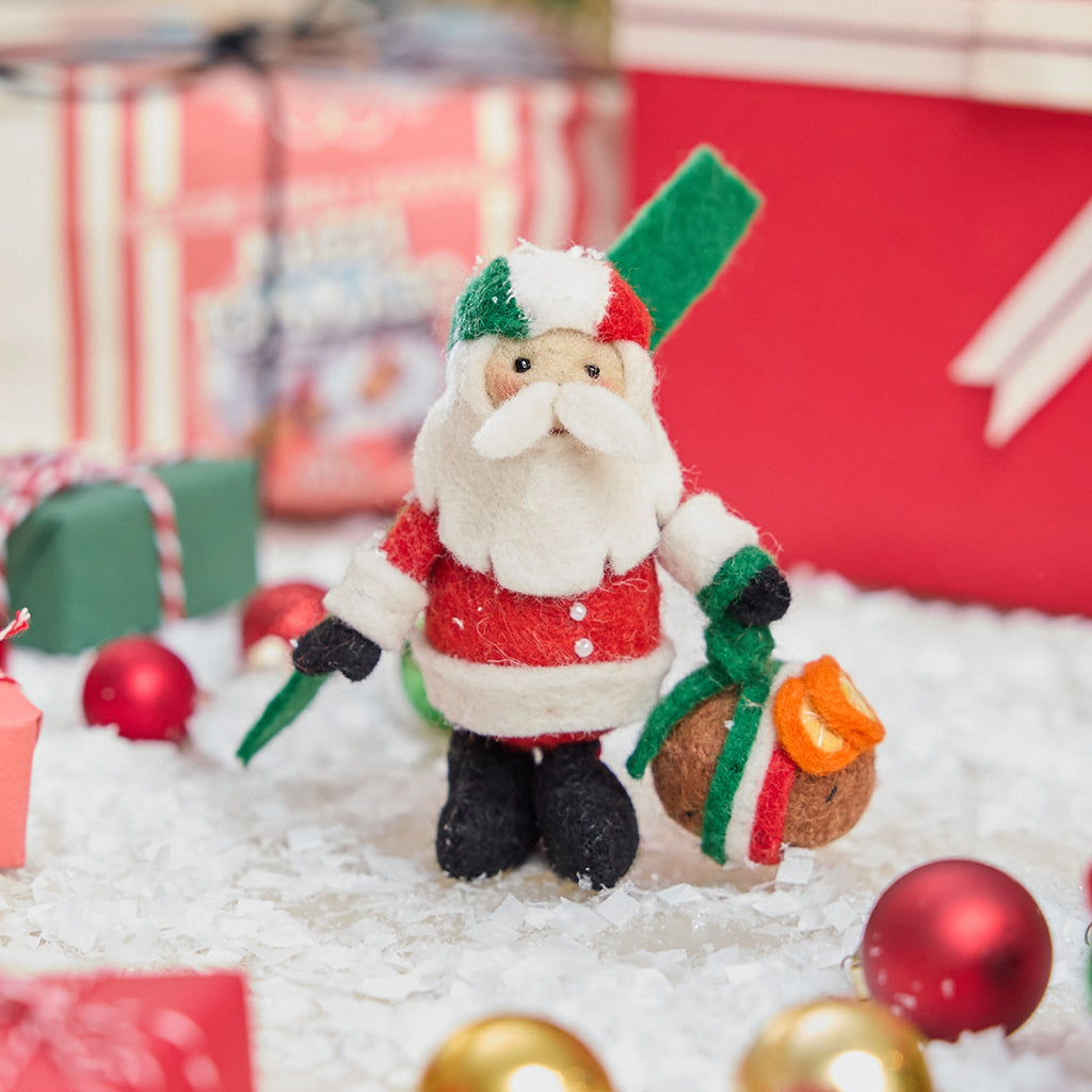 Craftspring’s handmade felt Italian Santa ornament — a cute Santa holding a panettone and wearing a helmet in Italian flag colors, displayed standing in snow with Christmas baubles and mini presents for a festive holiday scene, perfect for Christmas decorating or gifting, ethically crafted by artisans using sustainable wool.