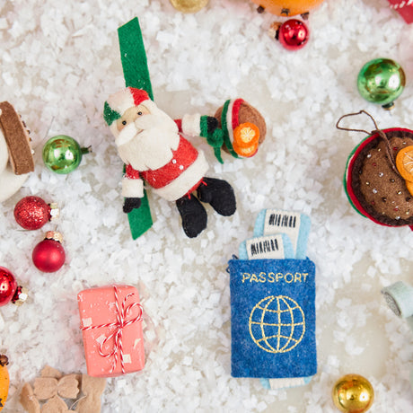 Craftspring’s handmade felt Italian Santa and Passport ornaments — a cute Santa holding a panettone and wearing a helmet in Italian flag colors, alongside a felt passport ornament, displayed in snow with Christmas baubles for a festive holiday scene, perfect for Christmas decorating or gifting, ethically crafted by artisans using sustainable wool.