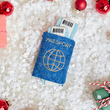 Craftspring’s handmade felt Passport ornament — featuring applique and embroidered details with two plane tickets tucked inside and passport stamps on the back, displayed with Christmas baubles and mini presents for a festive holiday scene, perfect for Christmas decorating or gifting, ethically crafted by artisans using sustainable wool.