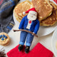Craftspring’s Canadian Santa Ornament — dressed in a denim jacket and jeans with ice skates, holding a hockey stick, and featuring a Canadian flag maple leaf — displayed alongside a stack of pancakes and Craftspring’s Blueberry Pancake Stack Ornament, evoking cozy holiday mornings, festive warmth, and heirloom-quality Christmas gifting, ethically crafted by artisans using sustainable wool.