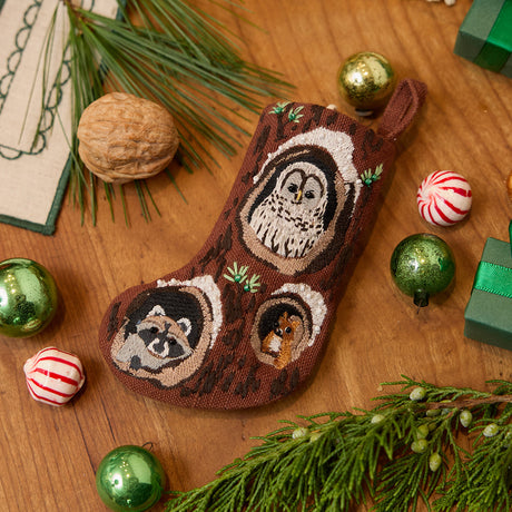 Craftspring’s handmade linen Woodland Mini Stocking ornament — featuring intricate beaded and embroidered details with an owl, raccoon, and squirrel peeking out of holes in a tree, displayed with evergreens, Christmas baubles, and peppermint candies for a festive holiday scene, perfect for Christmas decorating or gifting, ethically crafted by artisans using sustainable materials.