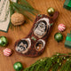 Craftspring’s handmade linen Woodland Mini Stocking ornament — featuring intricate beaded and embroidered details with an owl, raccoon, and squirrel peeking out of holes in a tree, displayed with evergreens, Christmas baubles, and peppermint candies for a festive holiday scene, perfect for Christmas decorating or gifting, ethically crafted by artisans using sustainable materials.