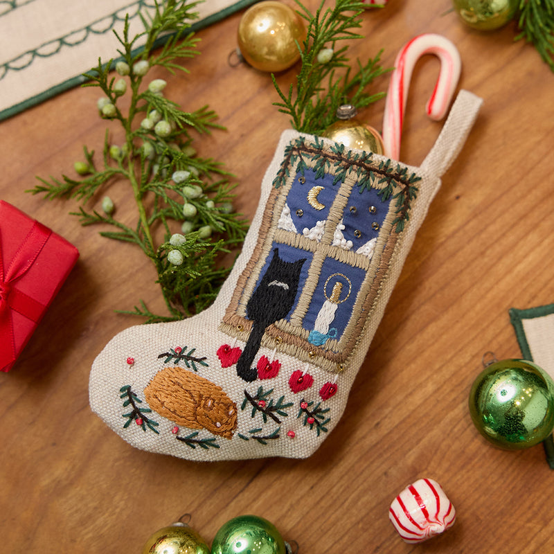 Craftspring’s handmade linen Holiday Cats Mini Stocking ornament — featuring intricate beaded and embroidered details of a cozy holiday scene with two cats and a window, displayed with evergreens, a mini candy cane poking out of the stocking, and Christmas baubles for a festive holiday scene, perfect for Christmas decorating or gifting, ethically crafted by artisans using sustainable materials.