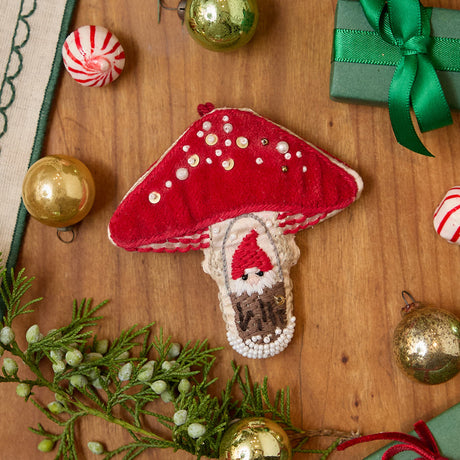 Craftspring’s handmade satin and velvet Mushroom Beaded Ornament — featuring intricate beaded and embroidered details with a gnome peeking out of a door on one side of the mushroom, displayed with Christmas baubles, peppermint candies, and mini presents for a festive holiday scene, perfect for Christmas decorating or gifting, ethically crafted by artisans using sustainable materials.