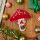 Craftspring’s handmade satin and velvet Mushroom Beaded Ornament — featuring intricate beaded and embroidered details with a gnome peeking out of a door on one side of the mushroom, displayed with Christmas baubles, peppermint candies, and mini presents for a festive holiday scene, perfect for Christmas decorating or gifting, ethically crafted by artisans using sustainable materials.