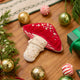 Craftspring’s handmade satin and velvet Mushroom Beaded Ornament — featuring intricate beaded and embroidered details with a gnome peeking out of a door on one side of the mushroom, displayed with Christmas baubles, peppermint candies, and mini presents for a festive holiday scene, perfect for Christmas decorating or gifting, ethically crafted by artisans using sustainable materials.