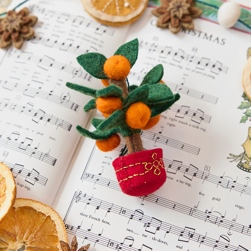 Clementine Tree Ornament from Craftspring displayed on sheet music with dried orange slices — handmade felt holiday decor with a red embroidered pot and clementines, festive for Christmas, Lunar New Year, and seasonal gifting, ethically crafted by artisans using sustainable wool.