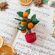 Clementine Tree Ornament from Craftspring displayed on sheet music with dried orange slices — handmade felt holiday decor with a red embroidered pot and clementines, festive for Christmas, Lunar New Year, and seasonal gifting, ethically crafted by artisans using sustainable wool.