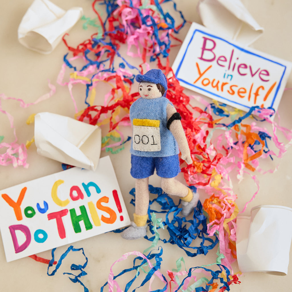Craftspring’s handmade felt Marathon Runner ornament — featuring a runner with a race bib numbered 001 and an armband, displayed with crushed paper cups, encouraging signs, and paper streamers for a playful race-day holiday scene, perfect for Christmas decorating or gifting, ethically crafted by artisans using sustainable wool.