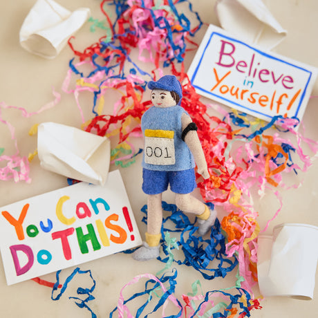 Craftspring’s handmade felt Marathon Runner ornament — featuring a runner with a race bib numbered 001 and an armband, displayed with crushed paper cups, encouraging signs, and paper streamers for a playful race-day holiday scene, perfect for Christmas decorating or gifting, ethically crafted by artisans using sustainable wool.