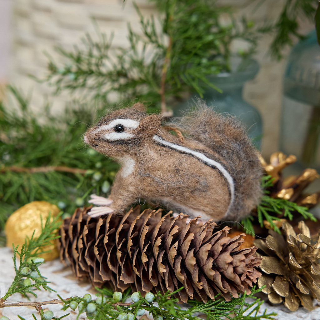 Craftspring’s Fuzzy Chipmunk ornament displayed standing on a pinecone among evergreens — handmade from sustainable wool with sweet needle-felted details and stripes, ethically crafted by artisans for Christmas decorating.