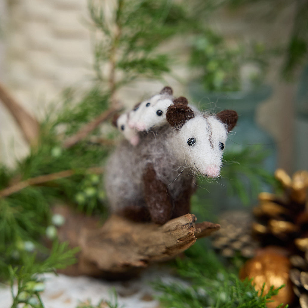 Craftspring’s Opossum Mom with Babies Ornament — handmade with three tiny babies with cute faces and pink tails — perched on a stick among evergreens, capturing whimsical holiday charm and heirloom-quality Christmas cheer, ethically crafted by artisans using sustainable wool.