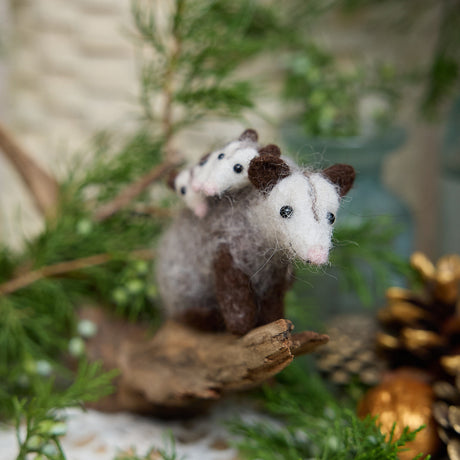 Craftspring’s Opossum Mom with Babies Ornament — handmade with three tiny babies with cute faces and pink tails — perched on a stick among evergreens, capturing whimsical holiday charm and heirloom-quality Christmas cheer, ethically crafted by artisans using sustainable wool.