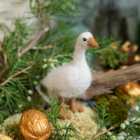 Craftspring’s Goose Ornament — handmade with fluffy feathers and beaded eyes — nestled on moss among evergreens and golden walnuts, evoking the cozy magic of holiday traditions and Christmas gifting — heirloom-quality decor, ethically crafted by artisans using sustainable wool.