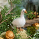 Craftspring’s Goose Ornament — handmade with fluffy feathers and beaded eyes — nestled on moss among evergreens and golden walnuts, evoking the cozy magic of holiday traditions and Christmas gifting — heirloom-quality decor, ethically crafted by artisans using sustainable wool.
