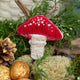 Craftspring’s handmade satin and velvet Mushroom Beaded Ornament — featuring intricate beaded and embroidered details with a gnome peeking out of a door on one side of the mushroom, displayed nestled among moss, evergreens, and golden walnuts for a cozy woodland holiday scene, perfect for Christmas decorating or gifting, ethically crafted by artisans using sustainable materials.