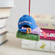 Lifestyle shot of the back of Craftspring’s Books Are Magic Hat with Books ornament, created in collaboration with the Books Are Magic bookstore—displayed with a stack of books for a festive holiday touch.