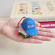 Lifestyle shot of Craftspring’s Books Are Magic Hat with Books ornament, created in collaboration with the Books Are Magic bookstore—held in hand above a stack of books, highlighting its whimsical holiday design.