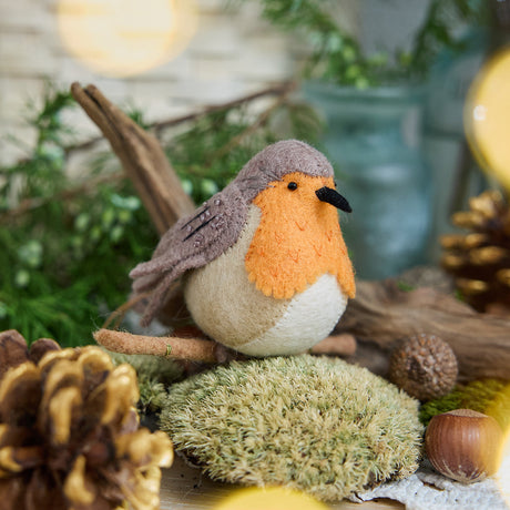 Craftspring’s handmade felt European Robin ornament — featuring delicate beaded and embroidered details, displayed perched on a stick surrounded by acorns, moss, and pinecones for a cozy woodland holiday scene, perfect for Christmas decorating or gifting, ethically crafted by artisans using sustainable wool.