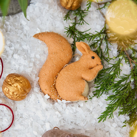 Craftspring’s handmade felt Red Squirrel ornament — featuring delicate beaded and embroidered details, displayed with evergreen branches and golden walnuts for a warm holiday scene, perfect for Christmas decorating or gifting, ethically crafted by artisans using sustainable wool.