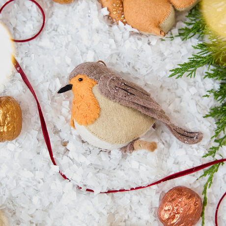 Craftspring’s handmade felt European Robin ornament — featuring delicate beaded and embroidered details, displayed with a red ribbon, evergreens, and golden walnuts for a festive woodland holiday scene, perfect for Christmas decorating or gifting, ethically crafted by artisans using sustainable wool.